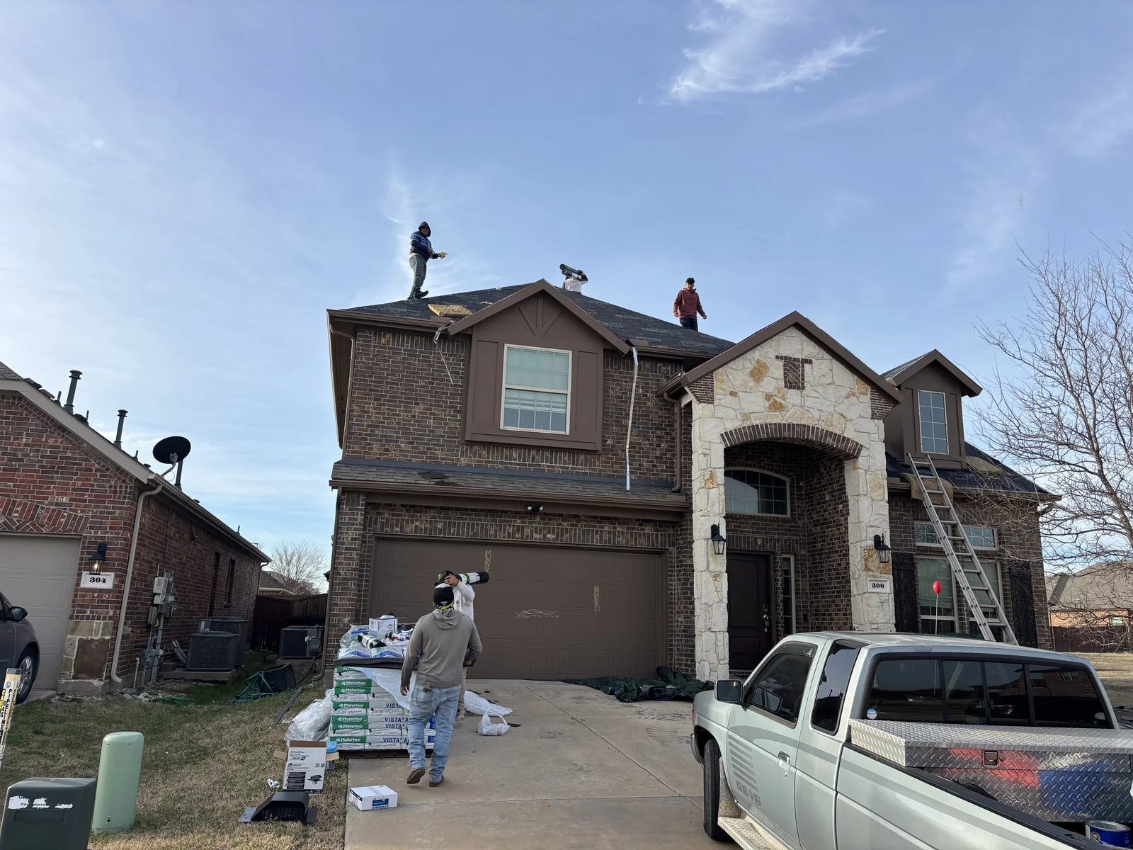 Roofing crew working on the Anna home, with shingle bundles staged in the driveway.