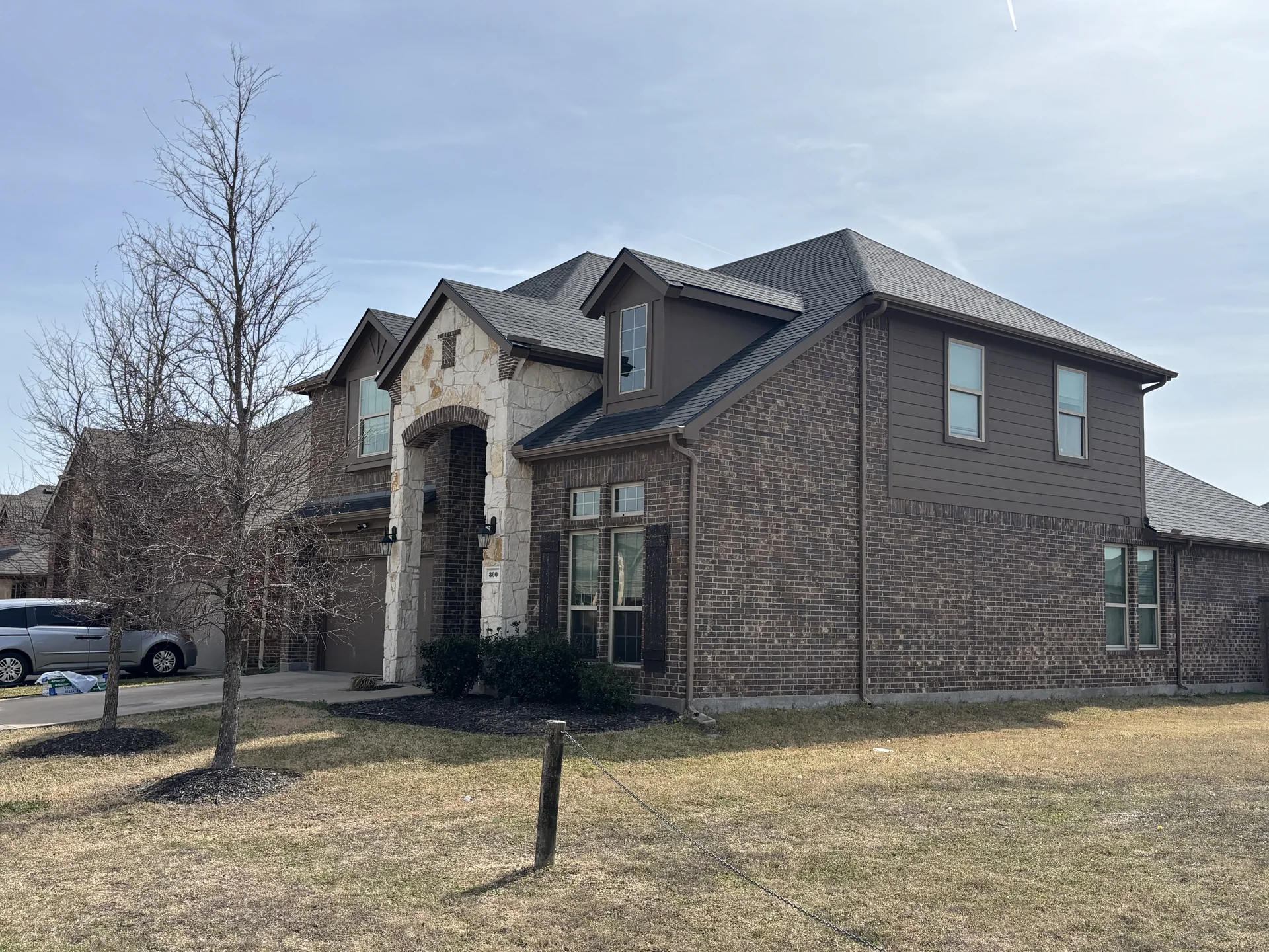 Completed Brilliant Black shingle roof on a two-story brick and stone home in Anna, TX, February 2026.