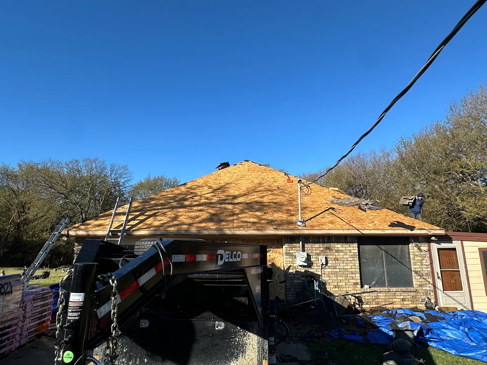 Exposed roof sheathing after tear-off, with a debris trailer beside the home.