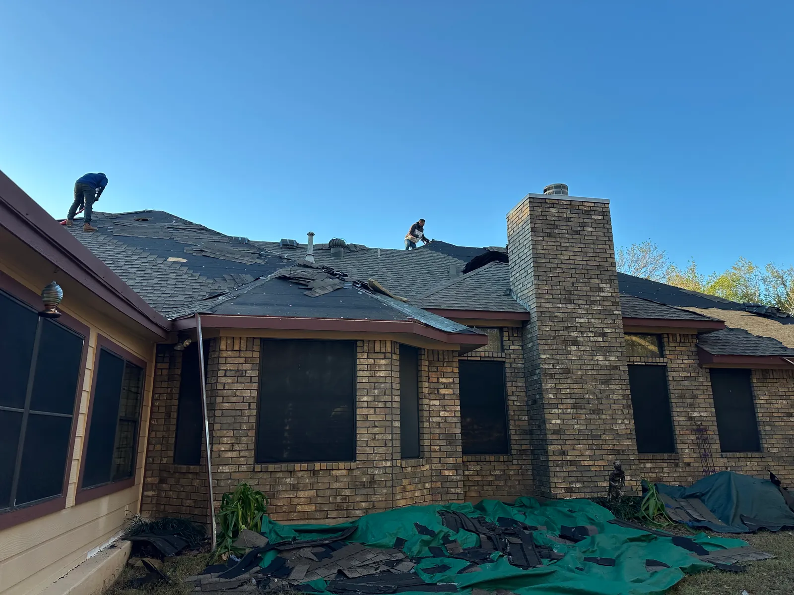 Crew removing old shingles around the rear chimney during the Denison reroof.