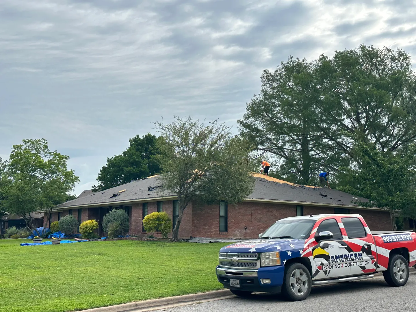 Crew preparing the Denison roof during tear-off, with the American Roofing truck in front.